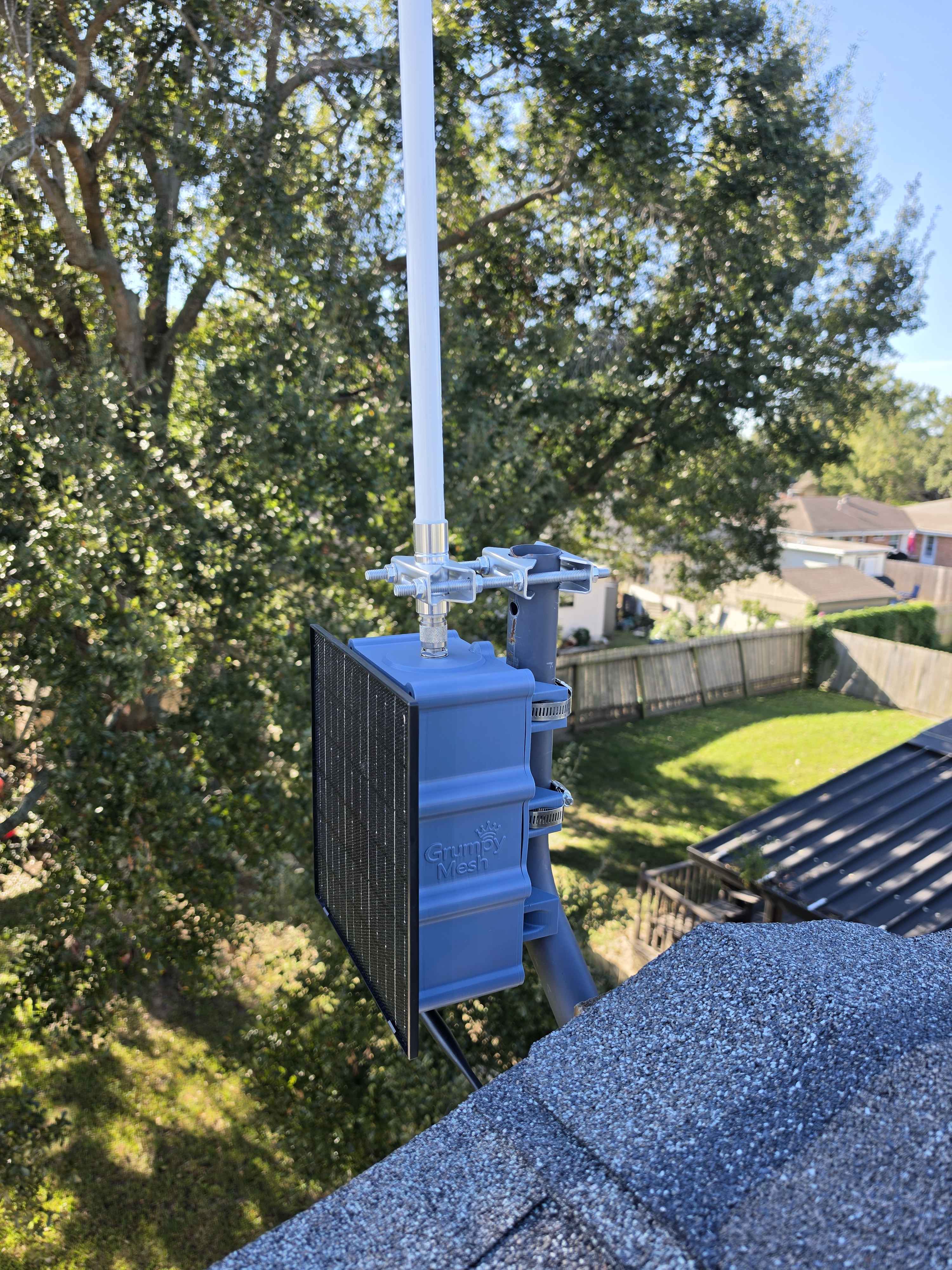 Blue GrumpyMesh repeater installed beside a rooftop with a tall antenna
