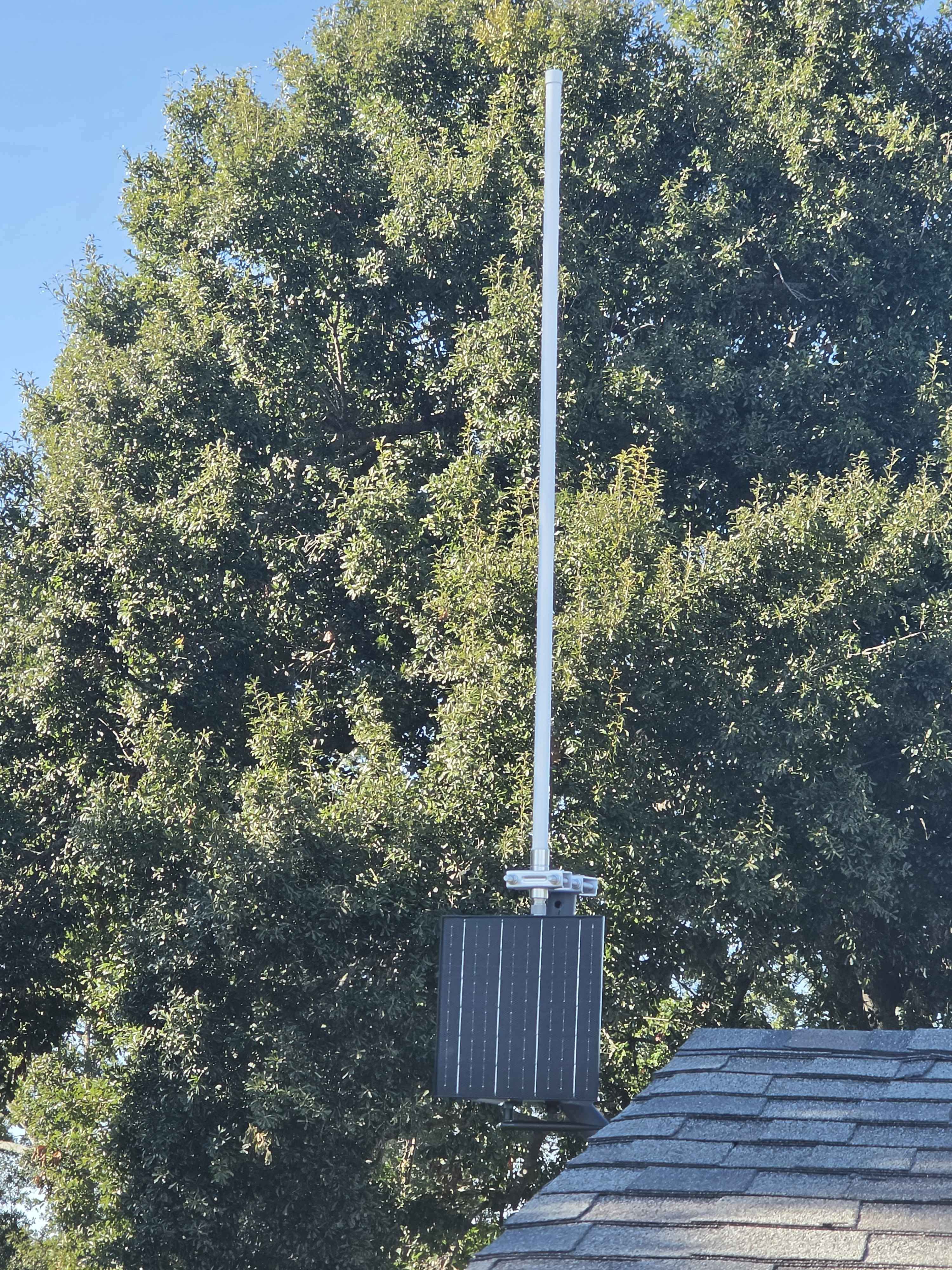 Solar repeater and antenna mounted near a roof with trees in the background